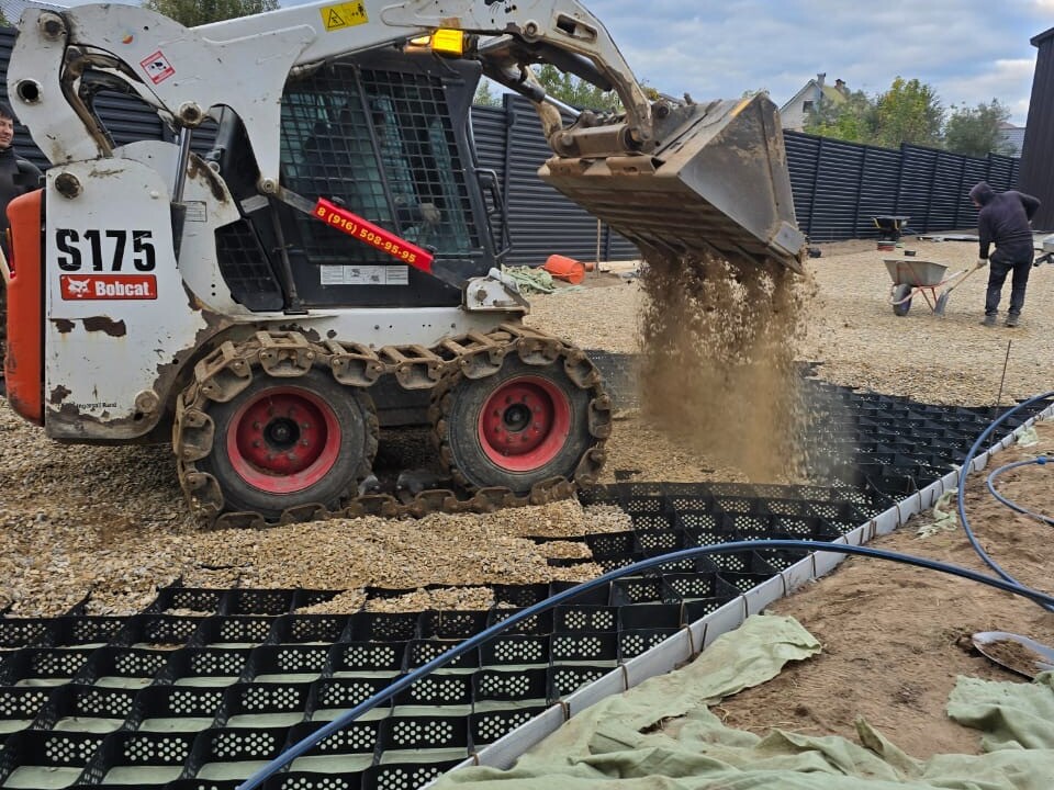 Мини-погрузчик Bobcat засыпает щебнем уложенную газонную решётку